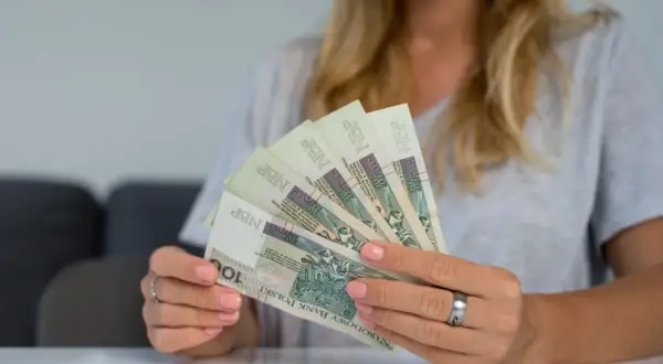 Kobieta trzyma w rękach banknoty 100 zł. To może być symbol dodatkowych 200 zł do emerytury za dzieci.