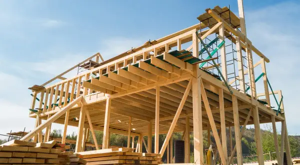 Estructuras de madera para casas en construcción, con vigas y soportes visibles bajo un cielo azul.