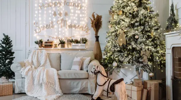 Ideas para decorar mi casa en navidad: árbol nevado, luces cálidas, sofá acogedor, caballito de madera y regalos.