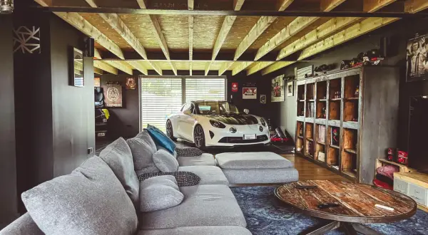 Aménager son garage : un canapé confortable, une voiture de sport blanche et des étagères remplies d'objets de collection.
