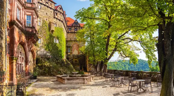 Zamek Książ w Wałbrzychu, z kamiennymi murami porośniętymi bluszczem, zaprasza do kawiarnianego ogródka pod rozłożystymi drzewami.