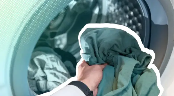 Hand lädt grüne Kleidung in eine Waschmaschine. Zeit, die neue Kleidung zu waschen und sie frisch zu machen.