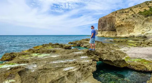 Hombre contempla el mar azul desde las rocas cerca del faro de Cabo de Gata. Acantilados y aguas cristalinas.