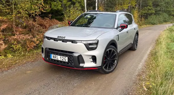 En smart 5-dörrars SUV i silver med röda detaljer kör på en grusväg genom en höstskog.