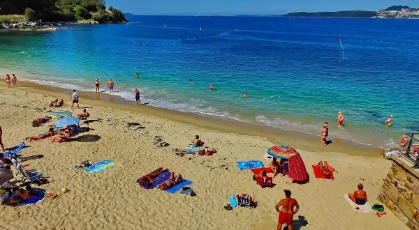 Gente disfrutando del sol y el mar en la playa Portocelo. Arena dorada, aguas turquesas y un día perfecto para relajarse.