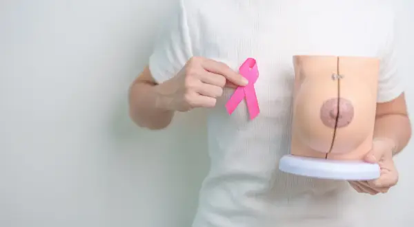 Dłoń trzyma różową wstążkę obok modelu piersi, symbolizując nadzieję po mastektomii z rekonstrukcją.