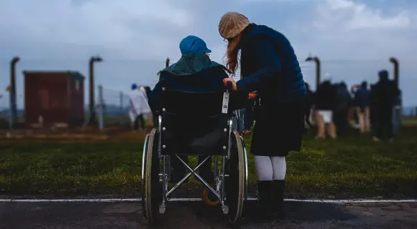 Donna assiste persona in sedia a rotelle, un momento di cura che ricorda l'importanza dell'indennità di accompagnamento dopo i 18 anni.