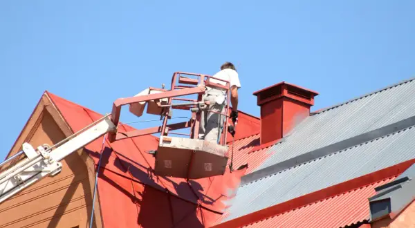 Pracownik na podnośniku maluje czerwony dach. Sprawdź, jaka jest malowanie dachu cena i odśwież wygląd swojego domu.