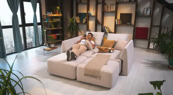 Mann entspannt auf einem modularen Sofa, das wie ein **Bett als Sofa gestalten** wirkt. Gemütliche Kissen und eine Decke laden zum Verweilen ein.
