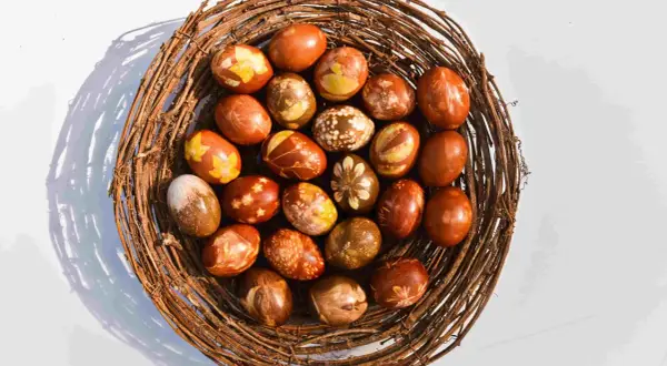 Pisanki w koszyku z gałęzi, barwione naturalnie w łupinach cebuli, z wzorami liści i kwiatów.