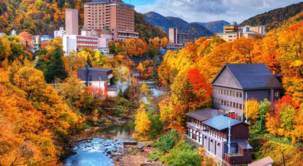 Town nestled in a valley with a river, surrounded by trees in vibrant autumn colors.
