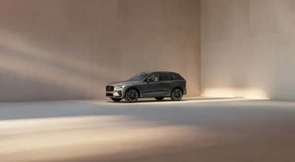 En mörkgrå Volvo XC60 står i ett ljust, minimalistiskt rum. Bilen visar upp sina eleganta linjer och fälgar, en perfekt representation av Volvo utrustningsnivåer.