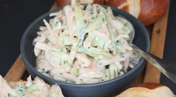 Ein cremiger Fleischsalat, perfekt für ein schnelles **Fleischsalat Rezept**. Serviert mit Laugenbrötchen.