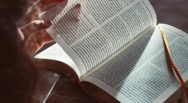 Osoba czyta Biblię, zgłębiając dogmaty wiary katolickiej. Światło podkreśla tekst, symbolizując oświecenie.