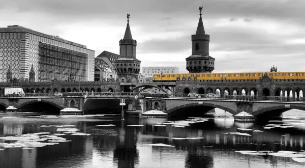 Gelbe U-Bahn fährt über die Oberbaumbrücke in Berlin. Im Vordergrund treibt Eis auf dem Wasser.