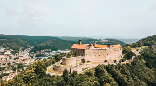 Die Plassenburg thront über der Kulmbach Altstadt, umgeben von grünen Hügeln. Ein malerischer Anblick!