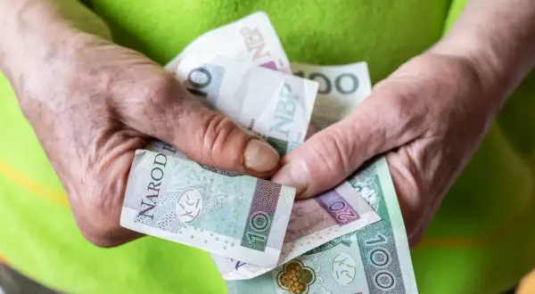 Dłonie starszej osoby trzymają polskie banknoty: 10, 20 i 100 zł.