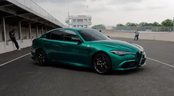 Zielona Alfa Romeo Giulia Quadrifoglio na torze wyścigowym, z wieżą kontrolną w tle.