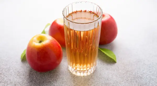 Glas mit Apfelsaft und Äpfeln. Über Apfelessig trinken Nachteile nachdenken.