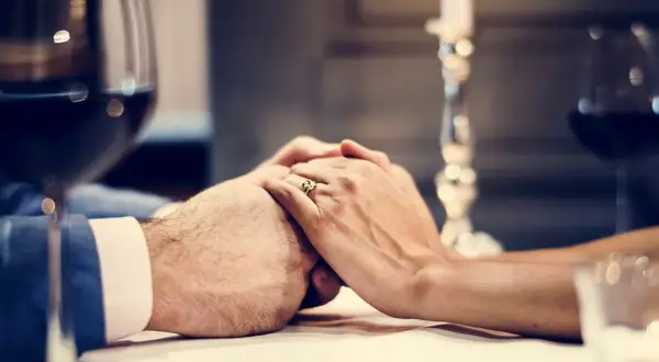 Dłonie splecione na stole, pierścionek na palcu. Romantyczna kolacja, idealna na 8 rocznicę ślubu.