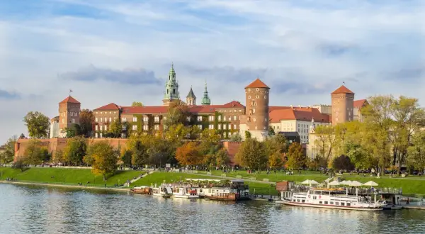 Zabytkowe miasto nad Wisłą, Wawel w jesiennej odsłonie, z łodziami cumującymi przy brzegu.