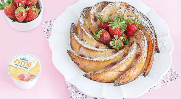 Torta di fragole e yogurt, soffice e profumata, decorata con zucchero a velo e fragole fresche. Accanto, una ciotolina di fragole e un vasetto di yogurt.