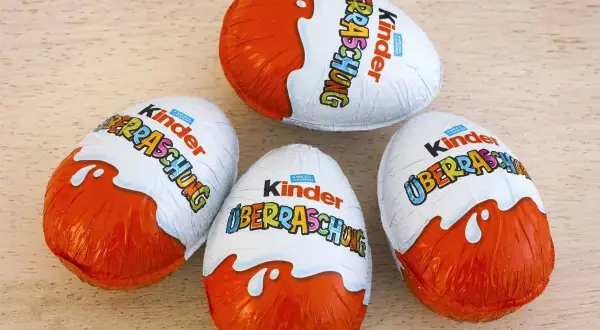 Cztery jajka Kinder Niespodzianka na drewnianym tle.