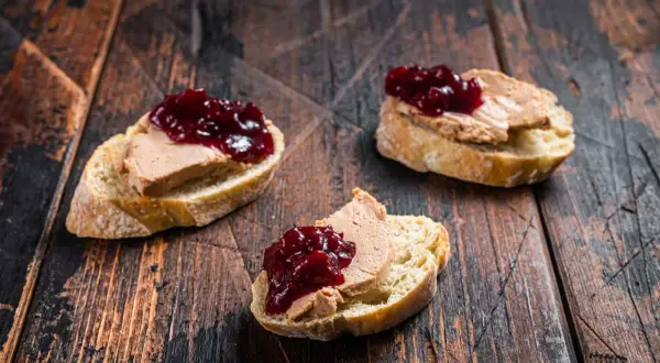 Trois toasts de pain de campagne garnis de foie gras et de confiture de fruits rouges. Un délice qui évoque le foie gras origine.
