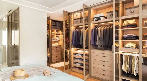 Armarios a medida con puertas de cristal y madera, llenos de trajes, ropa doblada y accesorios.