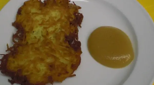 Zwei knusprige Kartoffelpuffer liegen auf einem Teller neben einem Klecks Apfelmus.