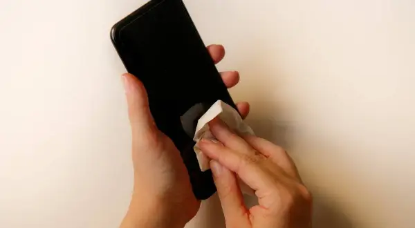 Dłonie czyszczą ekran telefonu chusteczką. Dowiedz się, czym wyczyścić ekran telefonu, by był lśniący i bez smug.