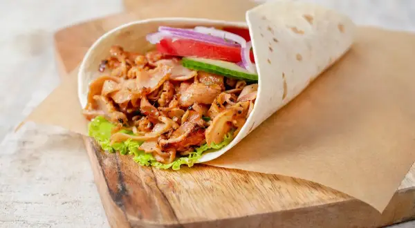 Domowy kebab w tortilli z mięsem, sałatą, pomidorem, ogórkiem i cebulą na desce.