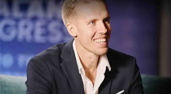 Uśmiechnięty mężczyzna, Dawid Piątkowski, w eleganckim garniturze. Wiek nie jest widoczny, ale jego energia jest wyczuwalna.