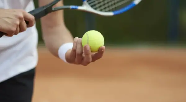 Gracz trzyma piłkę do tenisa ziemnego, gotowy do serwisu. Poznaj zasady gry w tenisa ziemnego i zacznij grać!