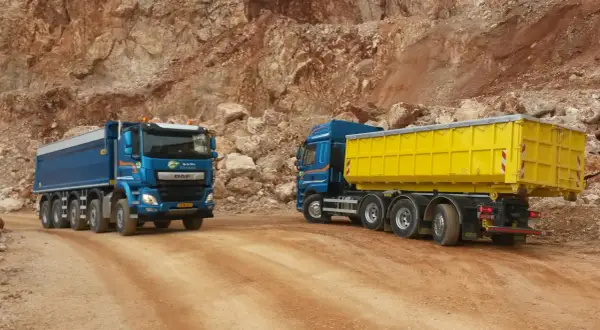 Deux camions bleus, un avec une benne jaune, circulent sur un chemin de carrière. Le prix du km camion 26 tonnes est une donnée clé pour ces transports.