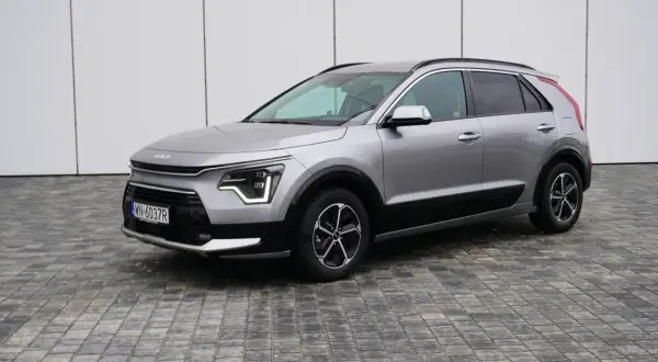Srebrny Kia Niro na tle białej ściany. Wiele osób szuka kia niro opinie przed zakupem.