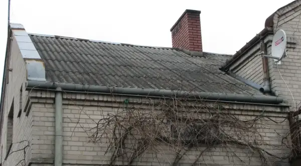 Dach pokryty eternitem, który zawiera azbest, z kominem i anteną satelitarną.