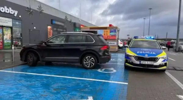 Czarny SUV zaparkowany na niebieskim miejscu dla niepełnosprawnych, obok radiowóz policyjny. To pytanie o to, jak długo można parkować na miejscu dla niepełnosprawnych, jest tu bardzo aktualne.