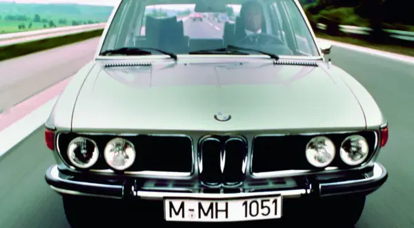 Klasyczne bmw e3 pędzi autostradą. Kierowca w garniturze pewnie prowadzi lśniący samochód.