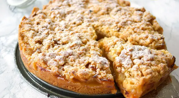 Saftiger apfelkuchen mit streusel, bestäubt mit Puderzucker. Ein Stück wurde bereits herausgenommen.