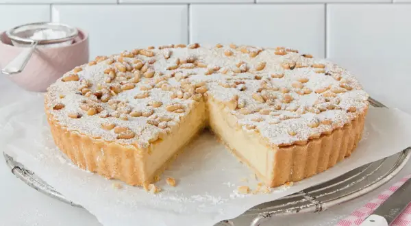 Eine köstliche Torta della Nonna, bestäubt mit Puderzucker und Pinienkernen, wartet darauf, angeschnitten zu werden.