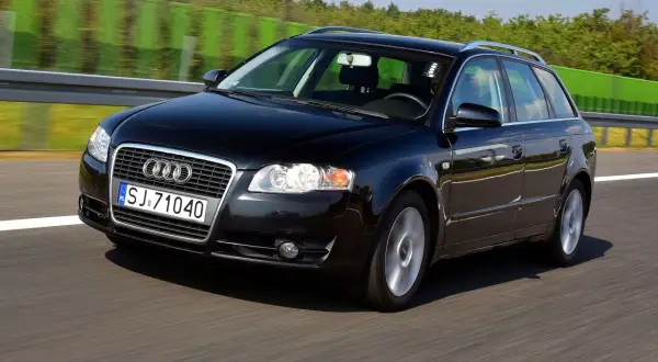 Czarne Audi A4 B7 2.0 TDI na autostradzie, z zielonymi barierami i drzewami w tle.