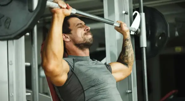 Mann hebt mit konzentriertem Gesichtsausdruck eine Langhantel im Fitnessstudio, ein intensiver 1 satz training.