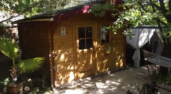 Charmante cabane en bois, nichée sous les arbres. Un hamac invite à la détente à côté.