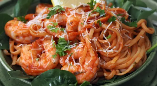 En skål med pasta pomodoro med räkor, toppad med riven ost och färsk persilja. En citronklyfta vilar ovanpå.