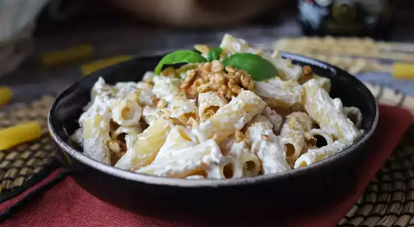 Makaron penne z kremowym sosem, orzechami włoskimi i bazylią w czarnej misce.