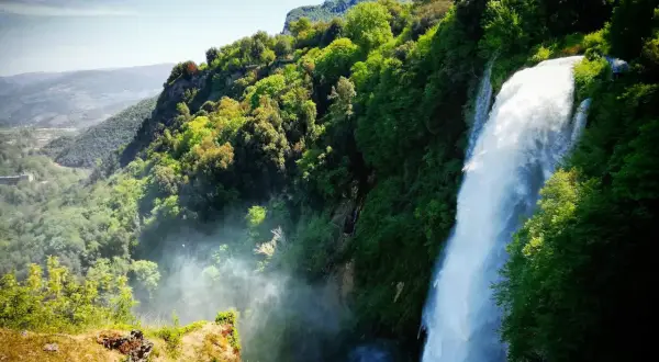 Cascata imponente nella rigogliosa montagna umbria, con valli verdi e cielo azzurro.