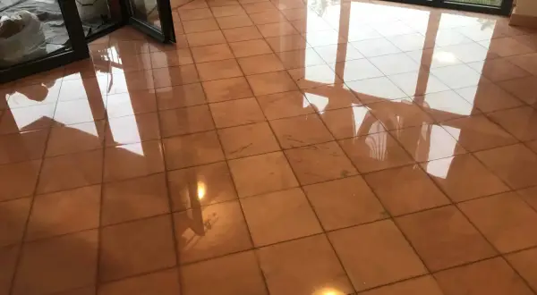 Pavimento in cotto lucido, riflessi di luce e finestre. Si intravede un secchio e sacchi, forse per pulire marmo con aceto.