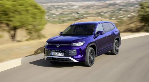 Fioletowy VW Tayron jedzie po krętej drodze wśród wzgórz.