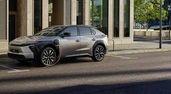 En silverfärgad elbil laddas vid en modern byggnad. En fråga som många ställer sig är: vad kostar det att ladda en hybridbil?